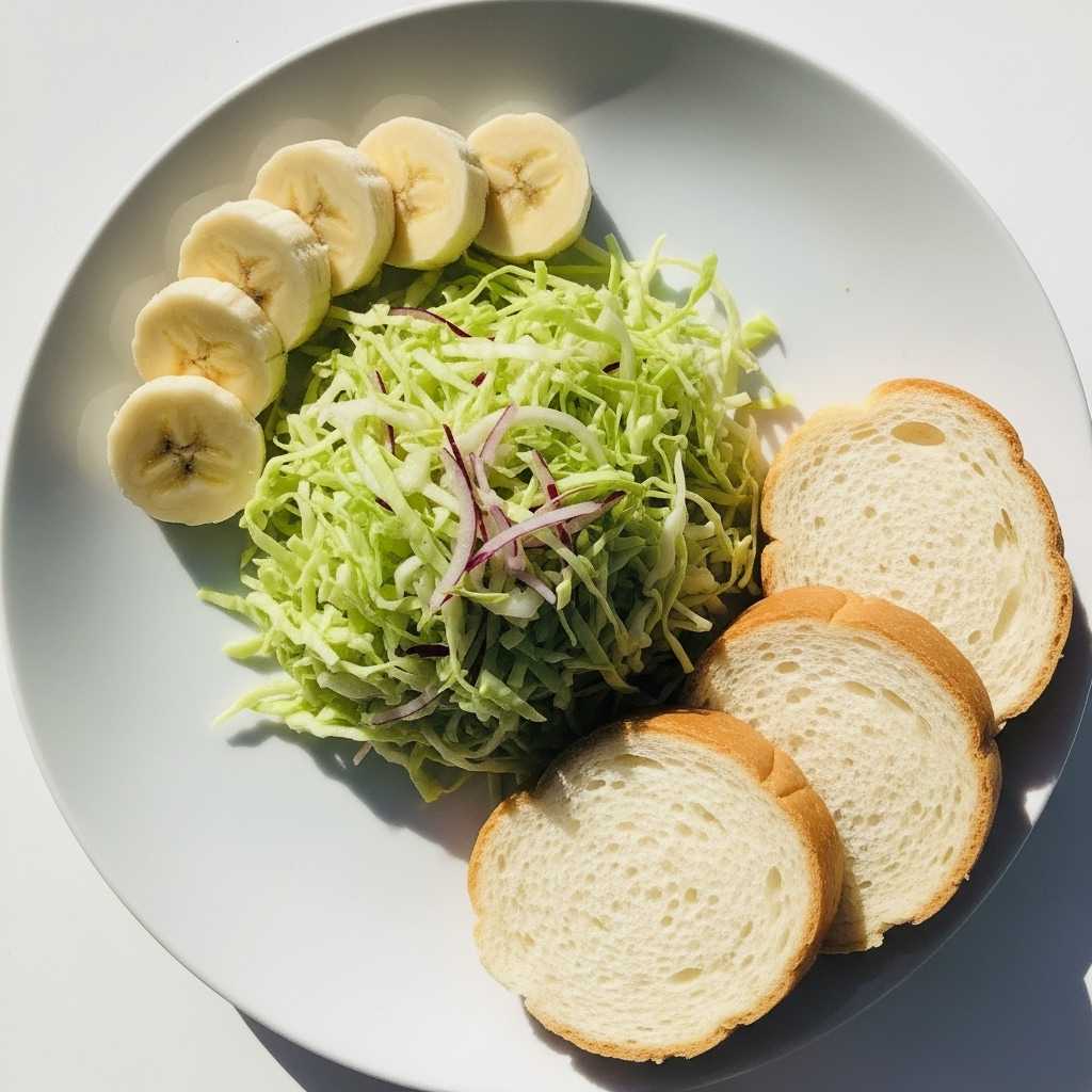 A top-down view of a meal with cabbage salad, bananas, and soft bread slices on a simple white plate, vibrant daytime light. 스트레스성 위염 증상, 이유, 그리고 효과적인 예방법 7가지