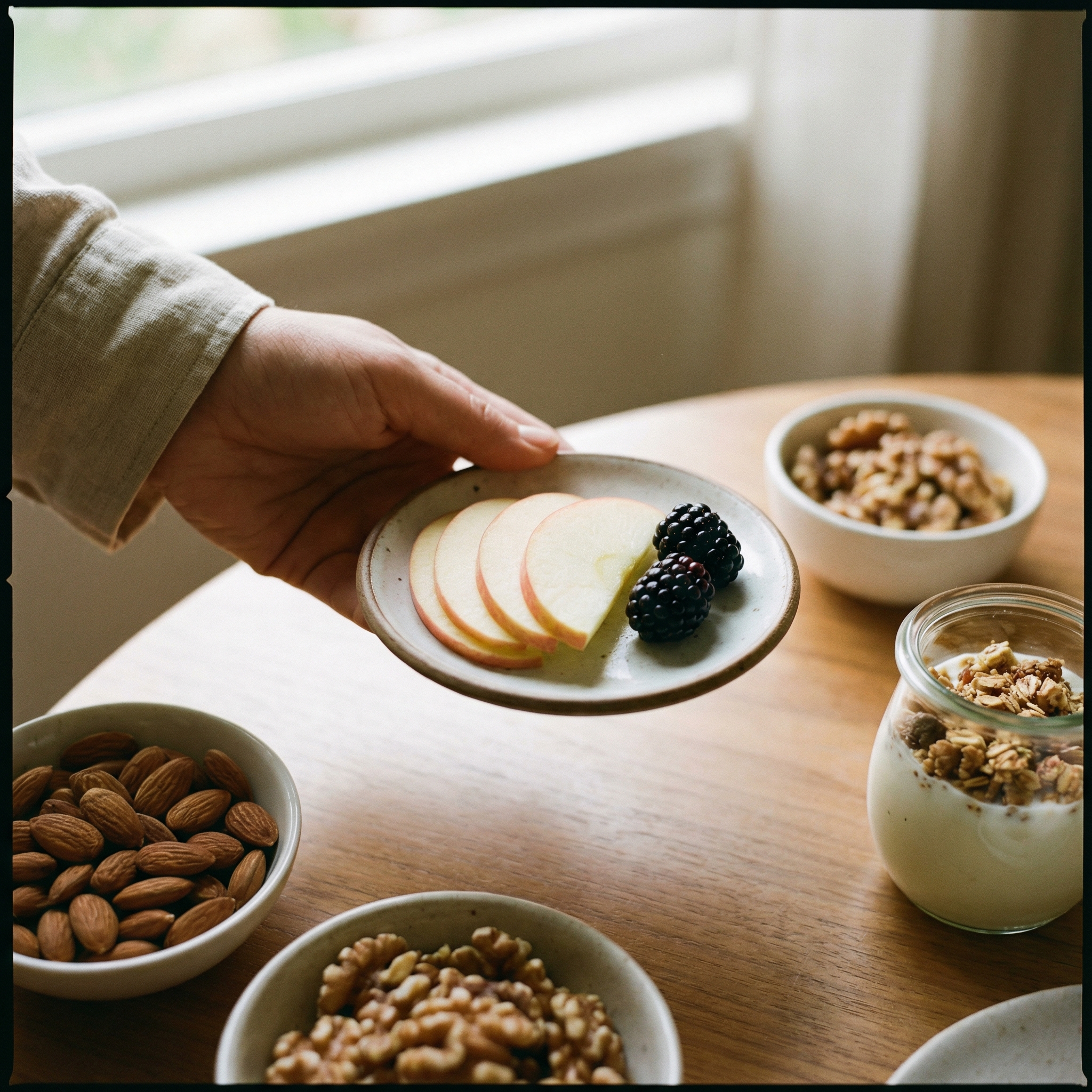 A close-up shot of a hand holding a portion of sliced fruit (e.g., a few apple slices or berries) on a small plate, with a background of healthy snacks like nuts or yogurt. Emphasize mindful portion control. Lifestyle photography, warm lighting. No visible text, 1:1 aspect ratio.